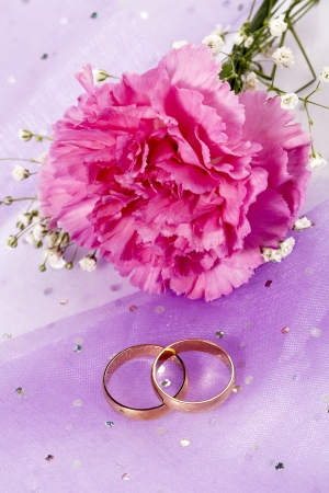 Close-up shot of two gold wedding rings and pink flower.の写真素材