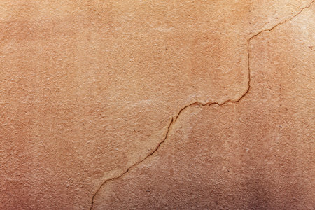 An orange wall made of stucco with a single crack that travels along the wall.の写真素材