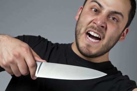 Close-up image of an angry male killer holding a knife over the gray backgroundの写真素材