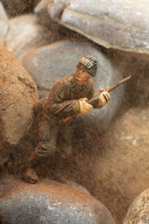 Miniature Toy holding a gun and hiding on dusty rocksの写真素材