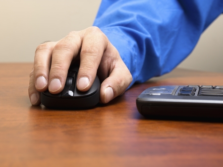Detailed shot of human hand holding optical mouse on wooden desk.の写真素材