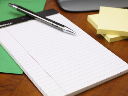 Detailed cropped shot of notepad and pen on wooden office desk.
