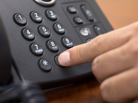 Close-up shot of human hand dialing number on black landline phone.の写真素材