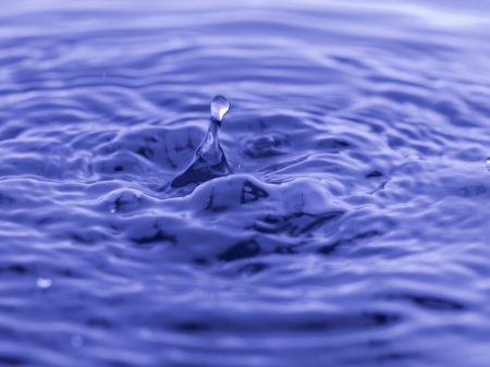 Closed up falling drop on water surface creating ripplesの写真素材