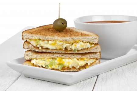Horizontal image of a scrambled egg sandwich with pierced olive fruit and tomato soup bowl on the sideの写真素材