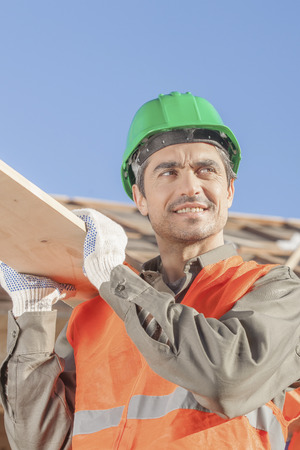 An orange vested laborer helping another carry a boardの写真素材