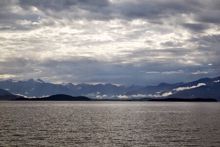 Beautiful morning view of the Mountain Range near Juneau Alaska from the water. Sun breaking through the cloudsの写真素材