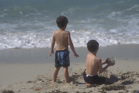 Two boys playing in the sand on a beach, close to the waterの写真素材