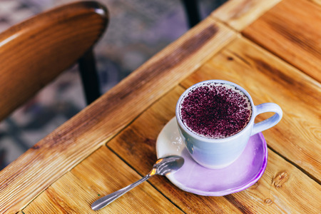 Lavender latte in a light purple cup on a wooden table. Lavender latte contains lavender flower tincture, espresso and blueberry powder. Flat, top view.の写真素材