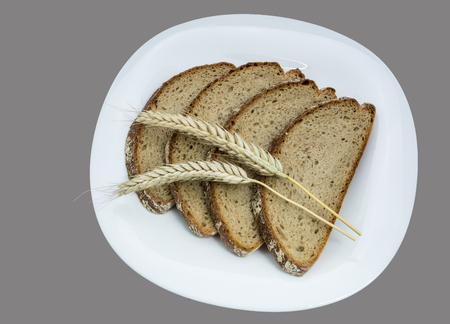 Bread and cereal spikes on a white plate. Four slices of bread with decorative dry barley. Isolated on gray background.の写真素材