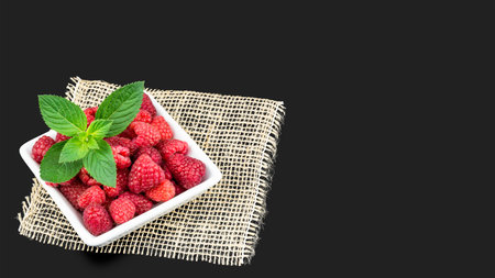 Delicious fresh raspberries on a dark gray background. Juicy red fruits in white square bowl with...