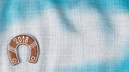 New Year horseshoe from Christmas gingerbread for good luck. Horseshoe with 2018 writing on background from blue wavy cloth with space for text.の写真素材