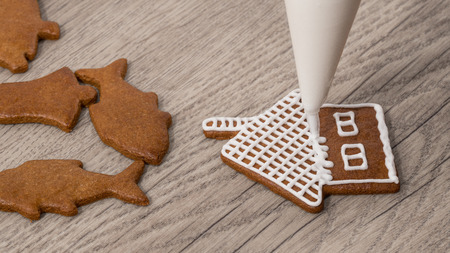 Close-up of decorating a christmas gingerbread in cottage shape. Painting of baked cookie using icing bag with sugar frosting on wood background.の写真素材