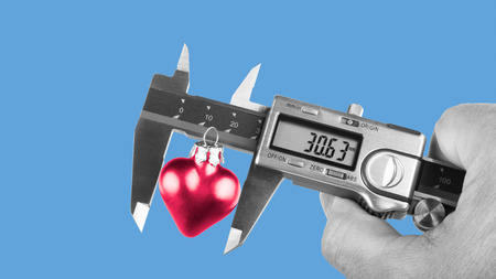 Black and white human hand holding a caliper when measuring a red heart. Idea for the size of love or its relation to science or technology. Isolated on sky-blue background.の写真素材