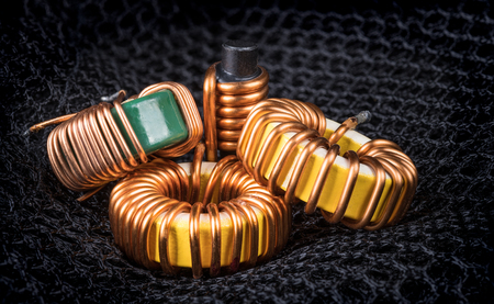 Group of coils with magnetic core and copper winding. Beautiful close-up of three toroidal inductors and one solenoid on background from black hexagonal mesh.の写真素材