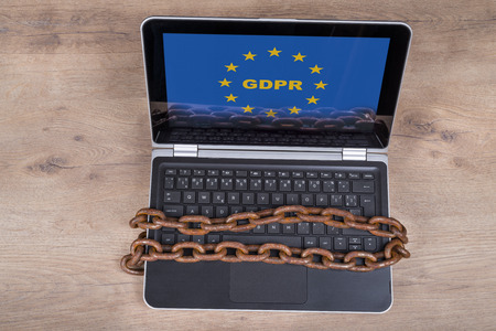 Laptop with GDPR letters in EU stars on wood background. Computer keyboard locked by rusty vintage chains. Idea of personal data protection, digitization and bureaucracy.の写真素材