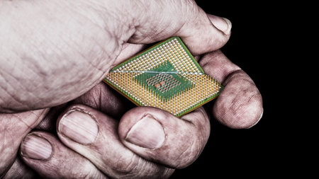 Dirty hand crushes microprocessor with critical bug. Broken computer chip in hacker's fist on black...