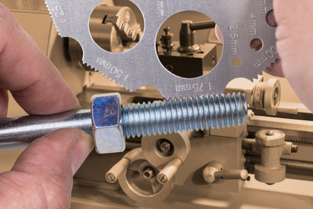 Measuring by screw pitch gauge with lathe in background. Measurement of thread on steel bolt with...