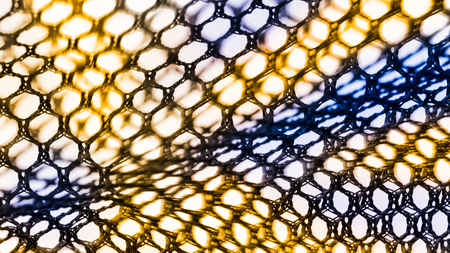 Abstract texture of net with hexagonal cells. Artistic detail of the decorative netting in black, yellow and blue color on white background. Concept of science, research, technology and industry.の写真素材