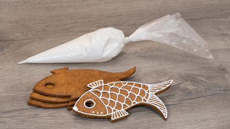 Christmas pastry and icing bag stacked on wood background. Close-up of traditional Xmas nad New Year gingerbreads in fish shape. Preparation for decorating a aromatic sweet cookies with sugar topping.の写真素材