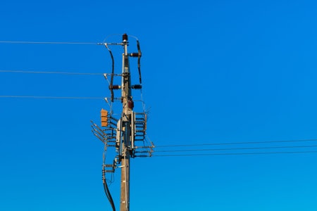 Medium voltage disconnectors on electricity pylon on blue sky background. Power line pole with...