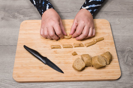 Baking sweet vanilla crescent rolls. Shaping of sliced raw dough on a wood cutting board. Female hands detail when making traditional Czech Christmas and wedding cookies. Aromatic nutty almond pastry.の写真素材