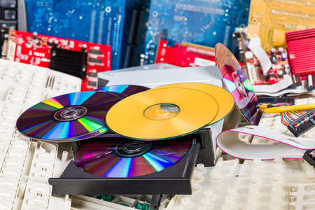 Disassembled computer hardware. Old compact discs on e-waste pile. Optical disks in DVD-ROM drive on...