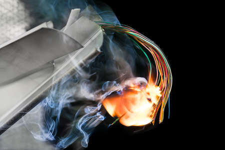 Flaming colored electric cables in damaged wreckages detail on black background. Fire of wiring in smoking metal or plastic parts. Concept of car or air crash, industrial accident or terrorist attack.の写真素材