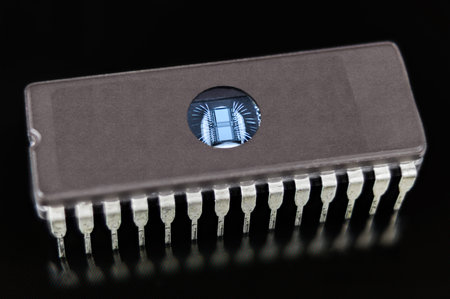 Erasable programmable read-only memory. EPROM chip on black background. Digital integrated circuit die with thin silver wires in DIP package with transparent window to erase data by ultraviolet light.の写真素材