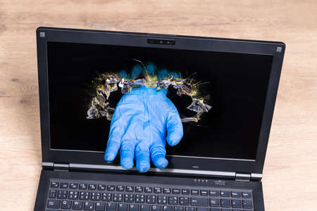 Laptop detail with imaginary helping hand in blue glove sticking out of punched hole in display. Online medical help idea. Symbolic virtual doctor. Distance health care concept in  disease.の写真素材
