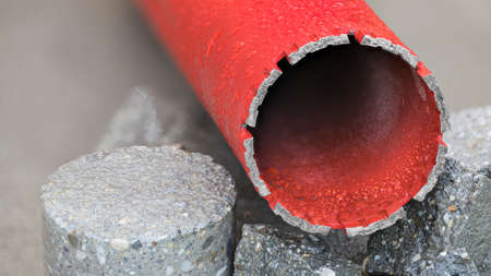 Red water cooled diamond core drill bit on round bored piece of gray concrete tile. Closeup of metal tube tool with attached sharp crown for wet drilling to masonry, stone and hard building materials.の写真素材