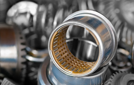 Closeup of needle roller bearing with plastic cylindric cage in steel bushing. Rolling metal part on blur background of pile of hardware components as gear wheel cogs or coil springs. Selective focus.の写真素材