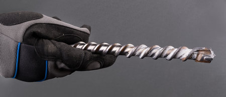 Hand with spiral fluted masonry drill bit with carbide tip on a gray background. Closeup of...