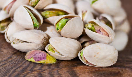 Closeup of roasted pistachio nuts with green cores in hard open shells. Pistacia vera. Beautiful detail of pistachios pile with salty flavor on brown wood. Yummy food with protein or healthy vitamins.の写真素材