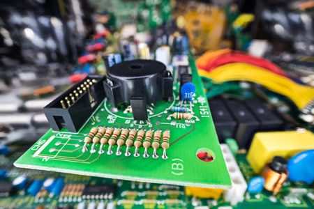 Various electronic components at green PCB in e-waste heap. Closeup of black piezoelectric buzzer,...