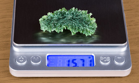 Closeup of beautiful green moldavite gemstone on weighing scale with digital display. Accurate weight determination of raw gem. Meteoric glass with rough wavy surface. Czech piece.の写真素材