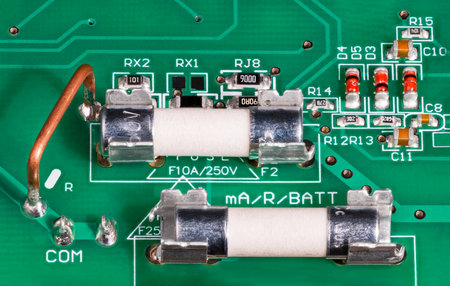 Ceramic electrical fuses in metal holder on circuit board. Low ohm wire resistor to current measuring, capacitors or red diodes. Surface mounted electronic components on green PCB.の写真素材