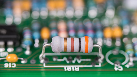 Close-up of white resistor with standard colored code on green printed circuit board. Electronic components with color band system on PCB with beautiful bokeh in blurry background.の写真素材