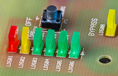 Closeup of colored LED lights and black button on beige printed circuit board. Green, yellow or red...