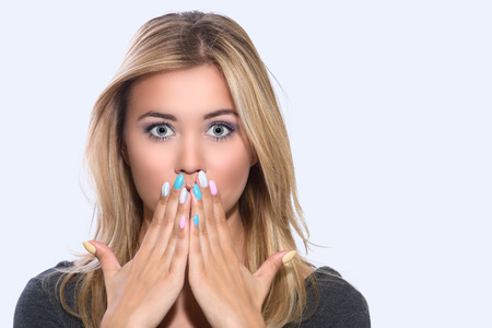 A vivid expression of emotion faces. Scared worried upset blonde. A young girl closes her mouth with her handsの写真素材