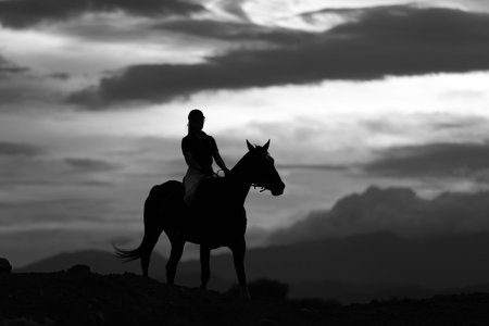 woman riding a horse in the courtyard on the mountain background Sky and sunset. Outdoor landscape in black and white tones in summer.の写真素材