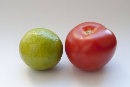 one red tomato and a green lime on a white backgroundの写真素材