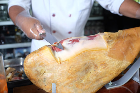 Chef cutting a piece of ham on a wooden board in a restaurantの写真素材