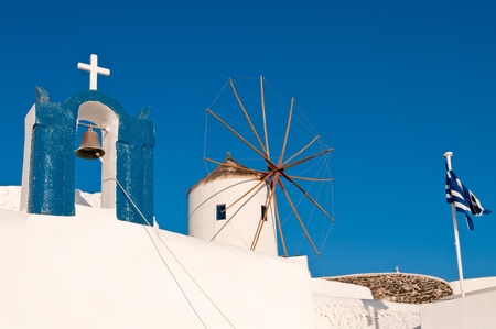 Church, windmill and greek flag in Oia, Santorini island of Greeceの写真素材