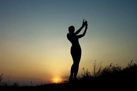 Silhouette of a young woman doing selfi at sunset sky backgroundの写真素材