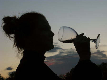 Silhouette of slim girl young woman female model sommelier with wine glass on nature over beautiful sunsetの写真素材