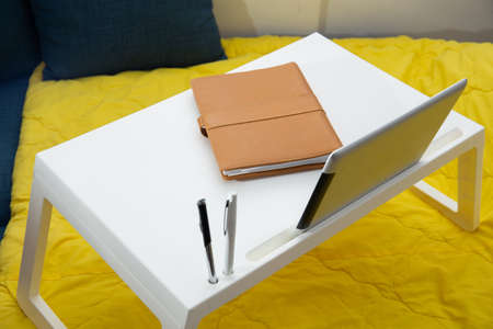 Work from home. Top shot of small table on bed with digital tablet , leather note book and penの写真素材