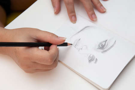 Close up shot of female hand drawing and sketching her face on notebookの写真素材