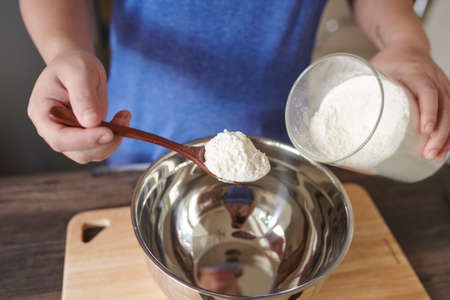 Photo of female hand using wooden spoon to pick up flour prepare for making cake on the tableの写真素材