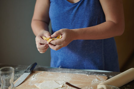 Front view of woman's hands making meat dumpling with wooden rolling pin. The process of making...